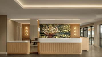 A reception area with a wooden reception desk, a large wall-mounted artwork, and a modern ceiling design.