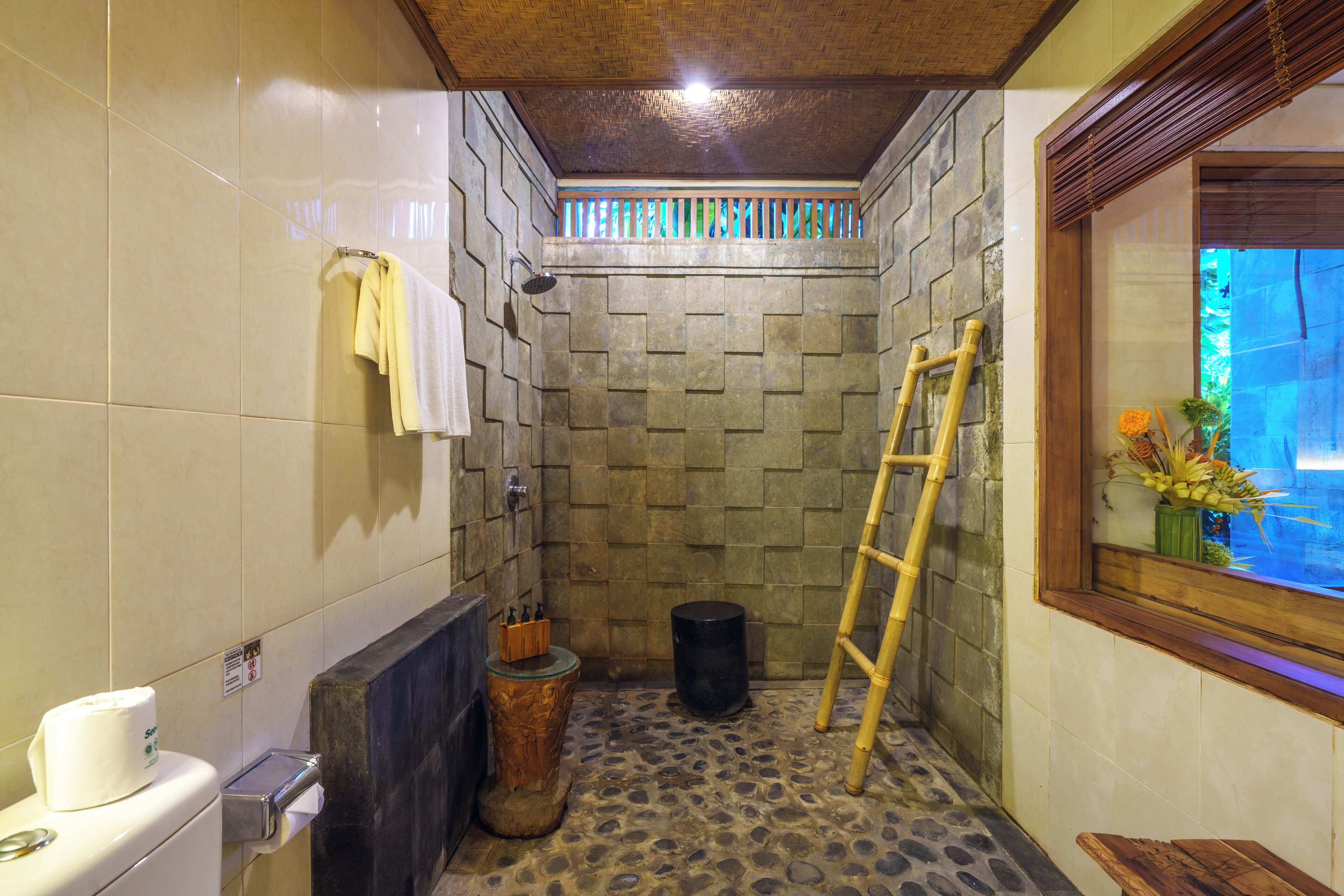 A bathroom with a stone wall, a wooden ladder, a toilet, and a window with a view.