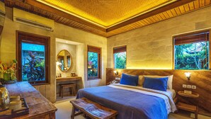 Un dormitorio con una cama grande, mesitas de noche, un tocador con espejo y ventanas con vistas al verdor.