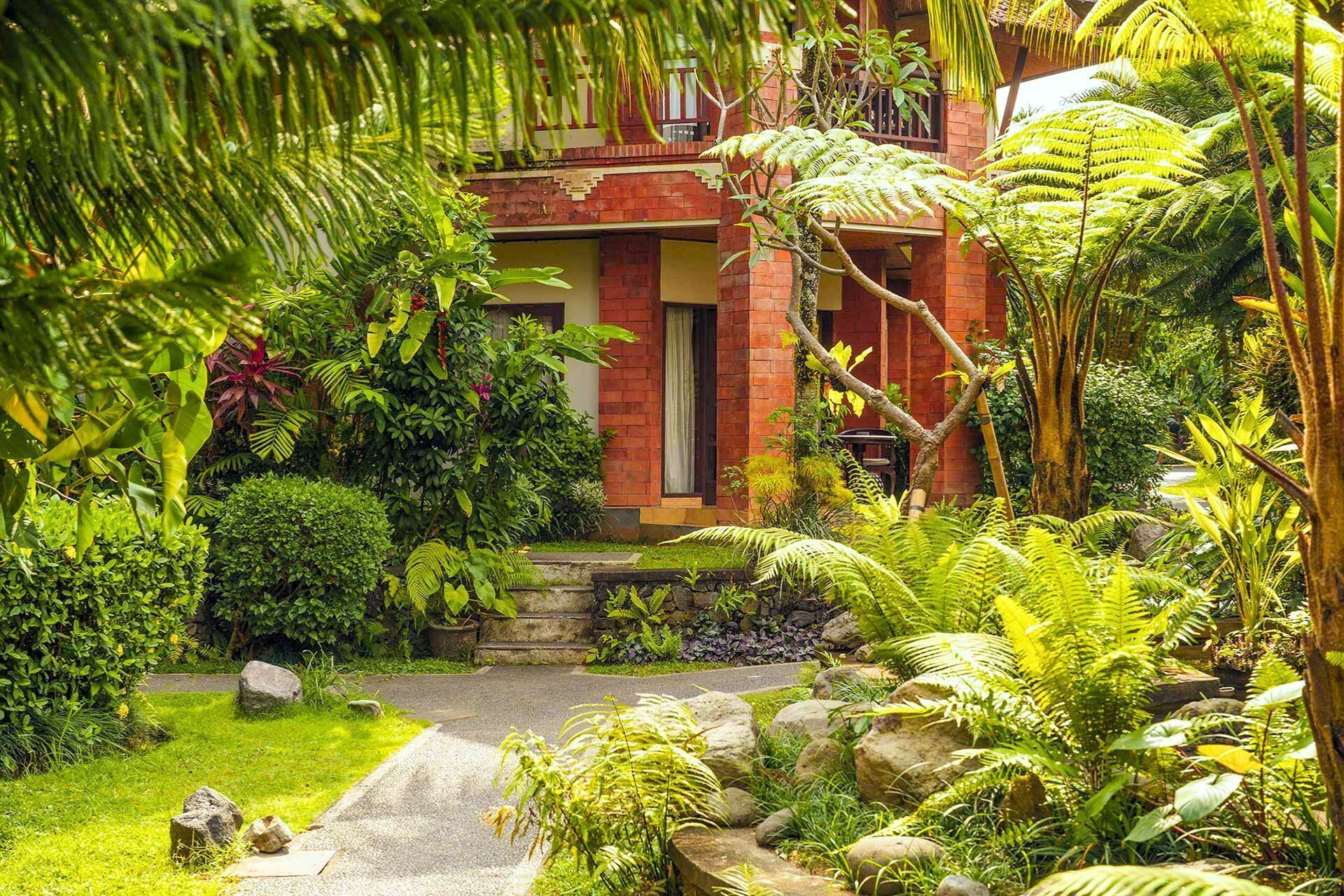 A lush garden with a pathway leading to a red brick building.