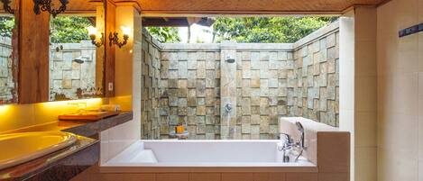 A bathroom with a large bathtub, a shower area with stone walls, and a wooden ceiling.
