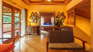 A room with a wooden ceiling, a bed with blue bedding, a table with a vase of flowers, and a chair. - Rama Phala Resort & Spa (Ubud)