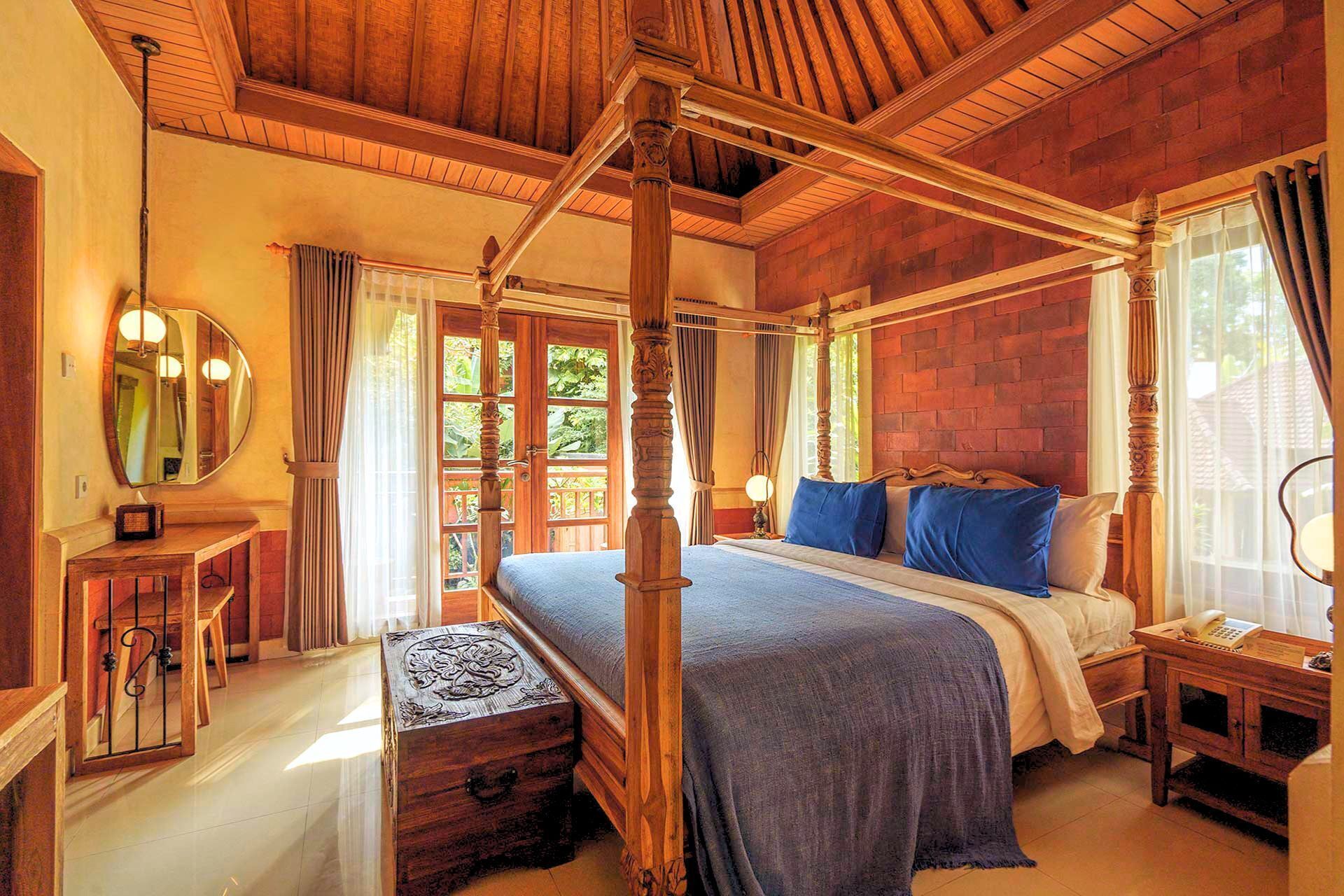 A four-poster bed with a wooden canopy, a bedside table with a lamp, and a large mirror on the wall.
