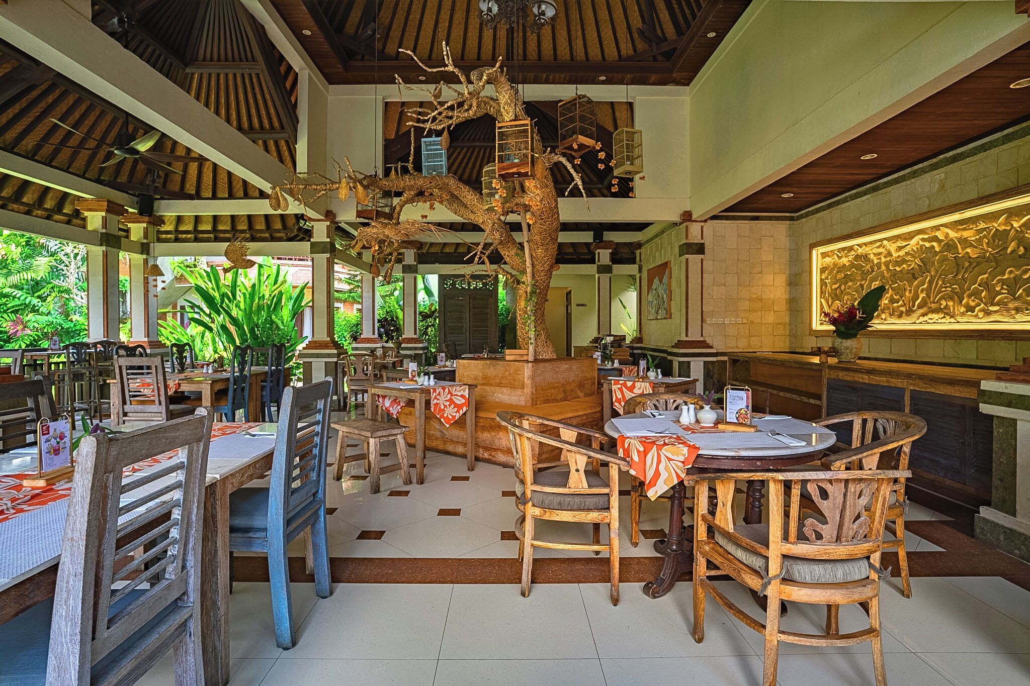 Ein Restaurant mit Holztischen, einer zentralen Baumskulptur und einem Fliesenboden.