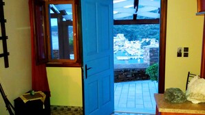 A room with a blue door leading to a balcony with a view of a coastal town. - Bilios Apartments (Fournoi)