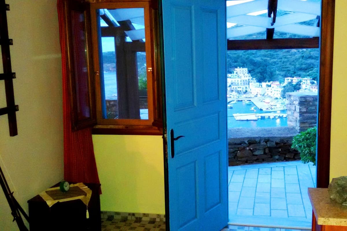 A room with a blue door leading to a balcony with a view of a coastal town.