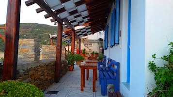 A covered outdoor seating area with stone walls, potted plants, and blue benches.