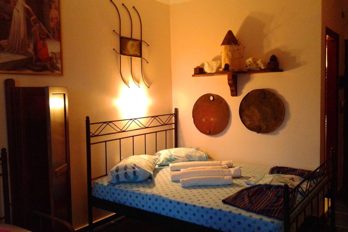 A bedroom with a bed, pillows, a wall-mounted shelf with decorative items, and a painting on the wall.