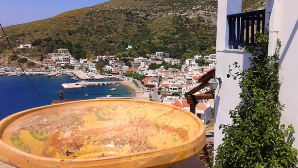 A coastal town with buildings, a harbor, and a mountain in the background. - Bilios Apartments (Fournoi)