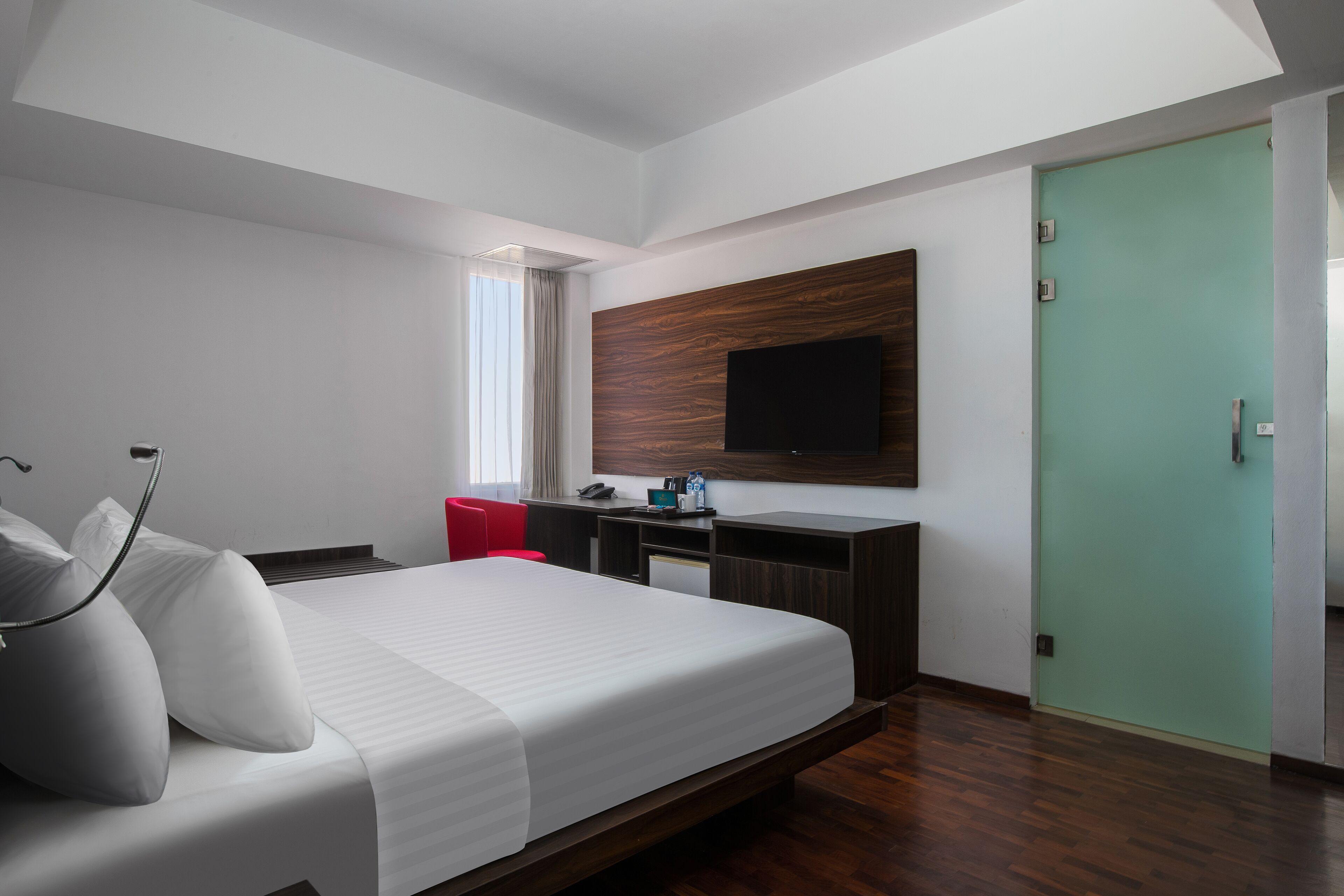 Habitación de hotel moderna con una cama grande, un escritorio, una silla, un televisor montado en la pared y una puerta verde.