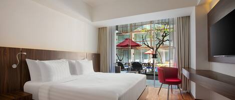 Habitación de hotel moderna con una cama grande, suelo de madera, televisor y vista a un área de estar exterior con sombrillas.