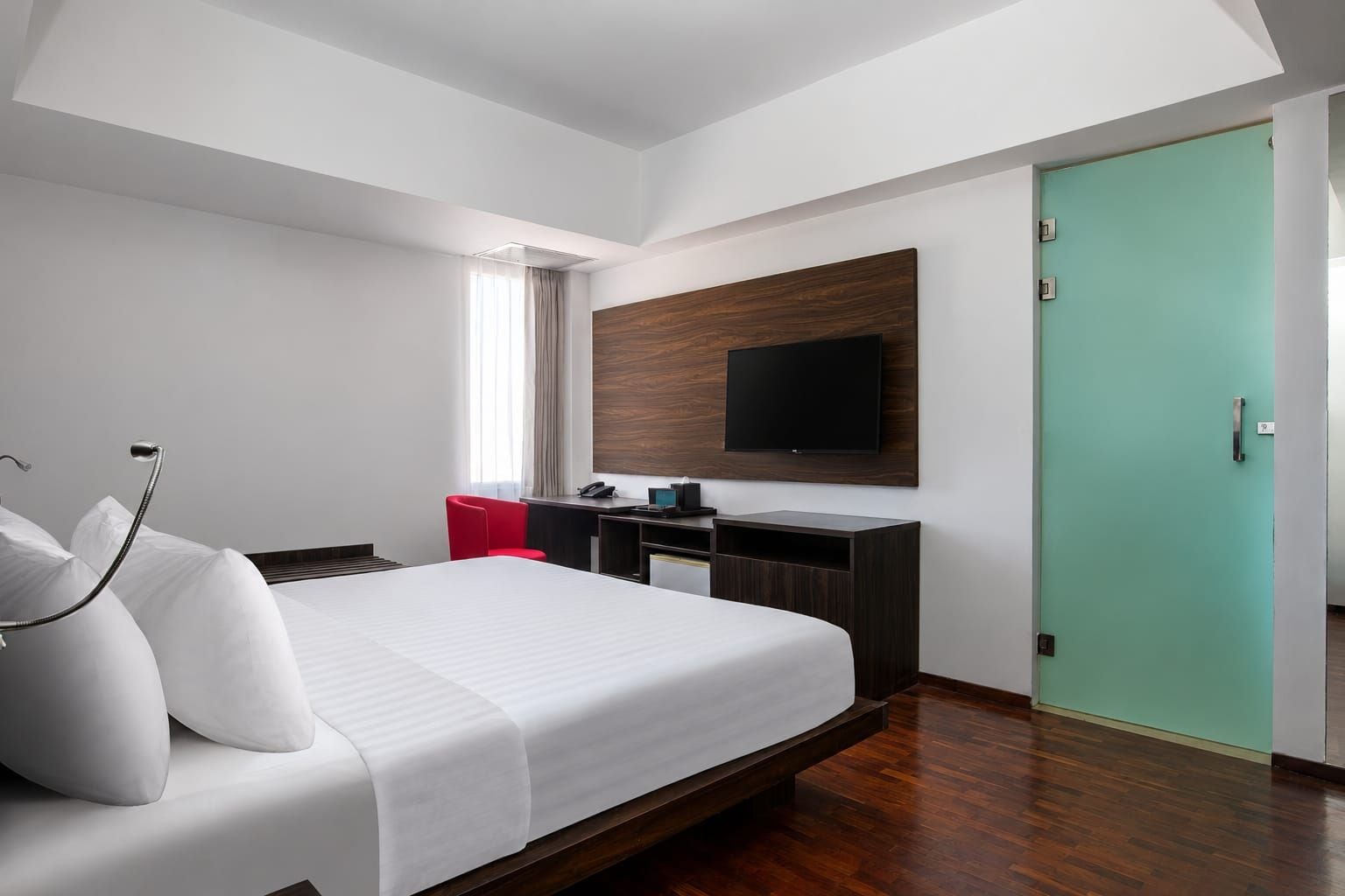 Una habitación de hotel moderna con una cama grande, un escritorio, un televisor de pantalla plana y una puerta verde.