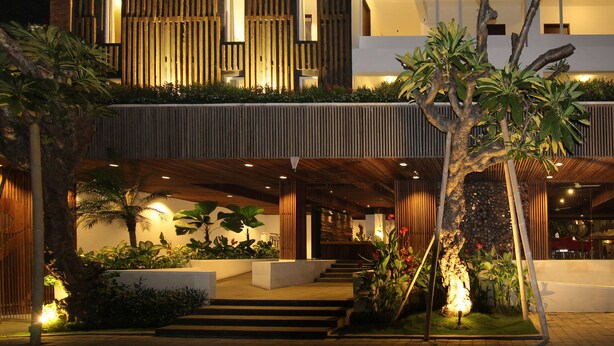 A modern two-story building with a well-lit entrance, a staircase leading to the upper level, and a variety of plants in the outdoor area. - The Bene Hotel (Kuta)