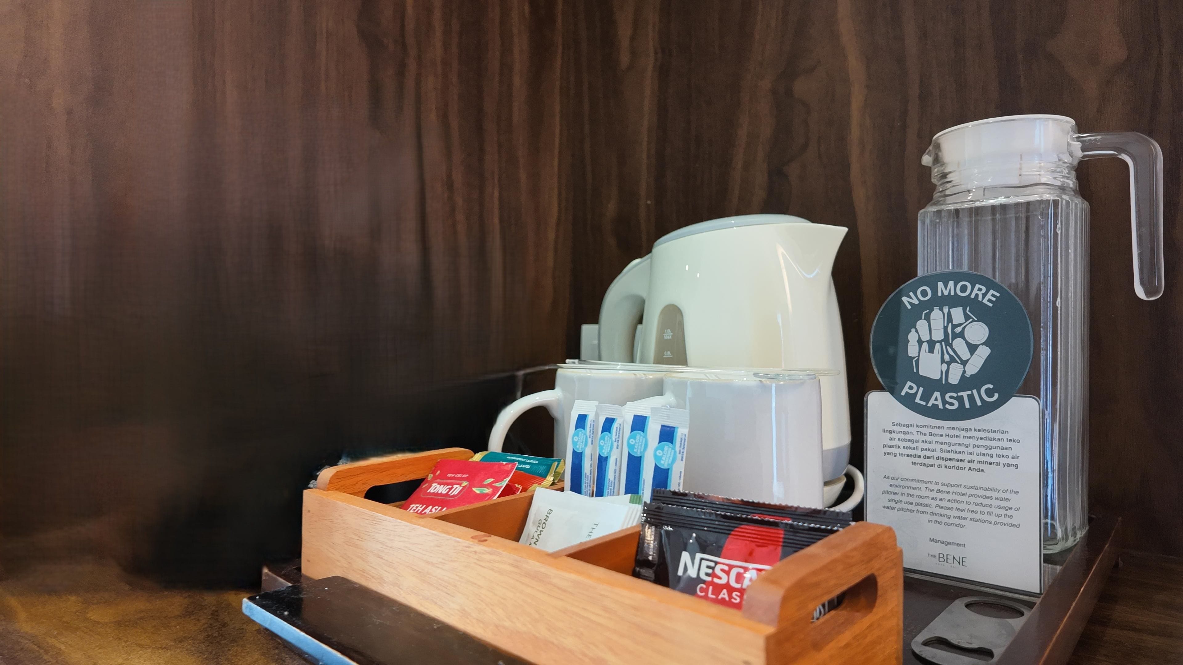 Les équipements d’une chambre d’hôtel comprennent une machine à café, un distributeur d’eau, un plateau avec des articles de toilette et un panneau indiquant « Plus de plastique ».