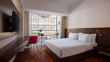 Ein modernes Hotelzimmer mit einem großen Bett, einem an der Wand montierten Fernseher, einer kleinen Essecke mit Tisch und Stühlen sowie Blick durch große Fenster.