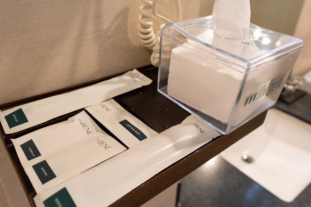 A tissue box on a hotel counter with tissue packets labeled 'The Bene' and 'Cotton Bud.'