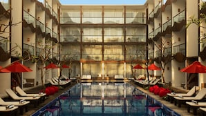 A modern hotel with a central swimming pool, multiple lounge areas with red umbrellas, and a multi-story building with balconies. - The Bene Hotel (Kuta)