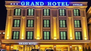 Exterior do Grand Hotel, com uma placa grande, várias janelas e um estacionamento cheio de carros.