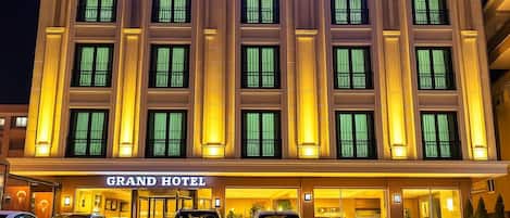 Das Grand Hotel mit auffälliger Beschilderung, zahlreichen Fenstern und einem Parkplatz mit Autos.
