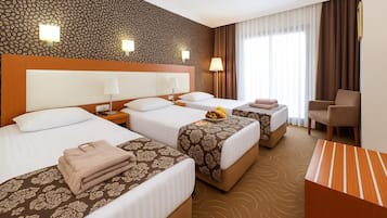 Ein Hotelzimmer mit drei Betten, einem Schreibtisch und einem Sessel.