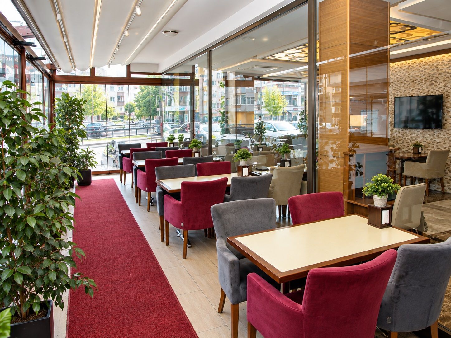 Uma área de refeições moderna em ambientes internos, com carpete vermelho, paredes de vidro e vista para a rua.