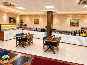 Ein Buffetbereich mit mehreren Tischen und Stühlen, einer zentralen Anrichte und verschiedenen Speise- und Getränkeausgabesystemen.