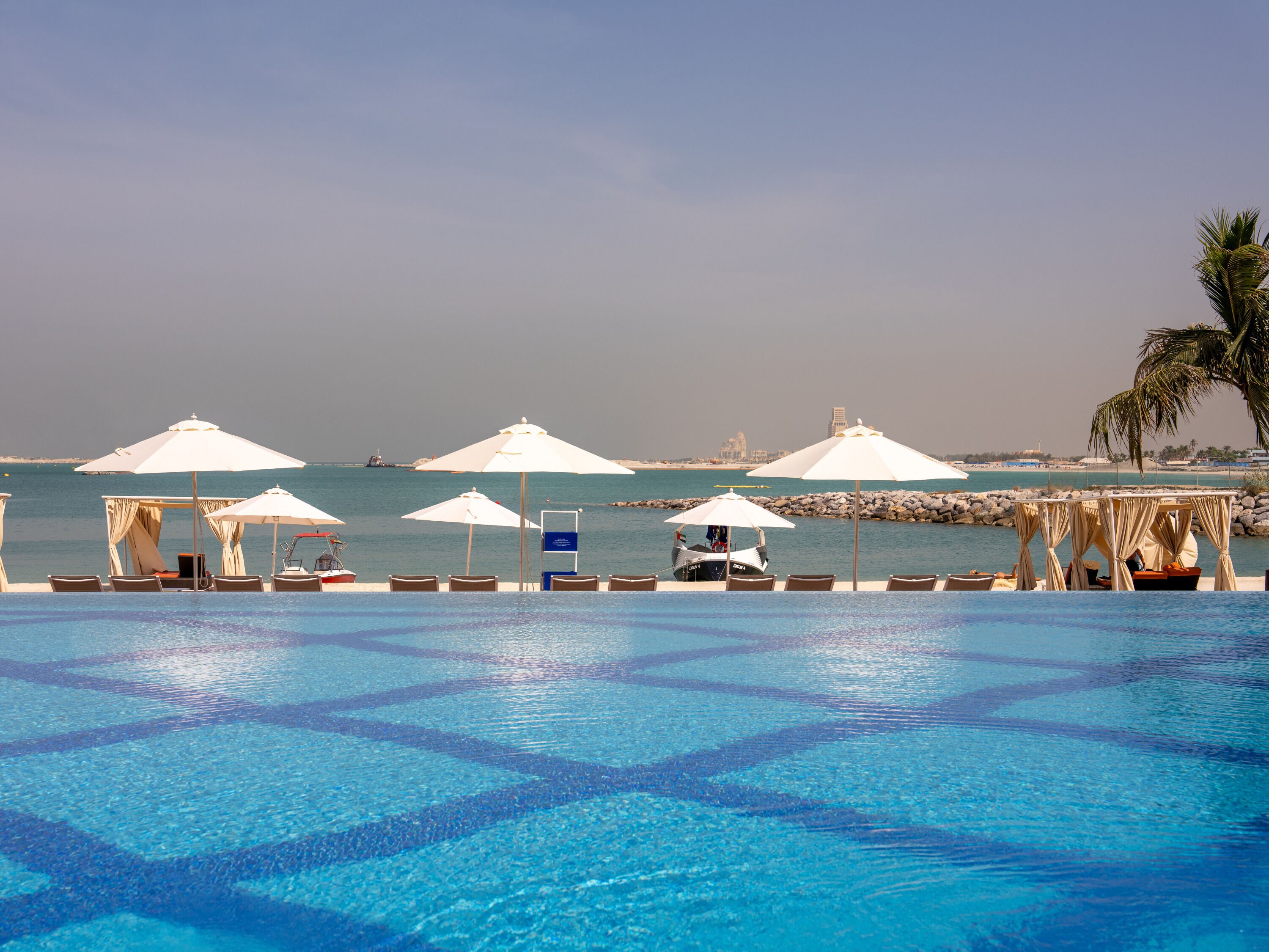 Ein Poolbereich mit Sonnenschirmen, Liegestühlen und Blick auf das Meer.