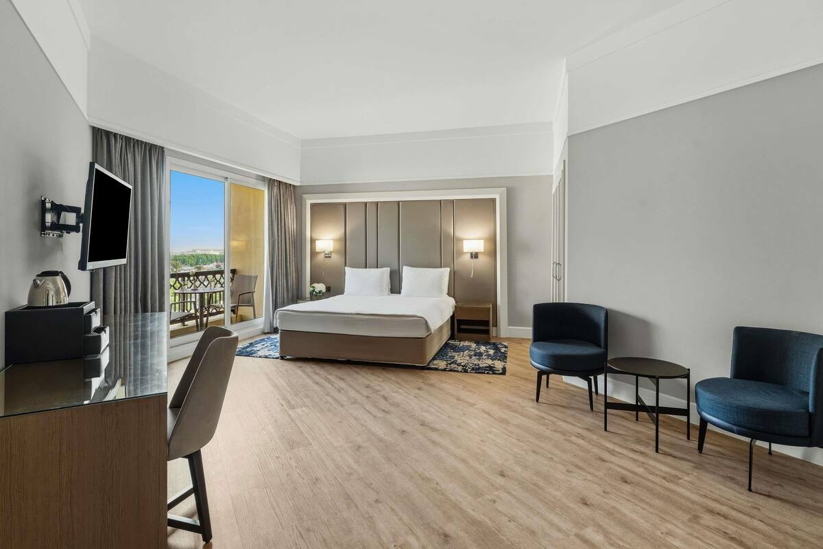 Una habitación de hotel moderna con una cama grande, un escritorio, un televisor y un balcón con vistas.