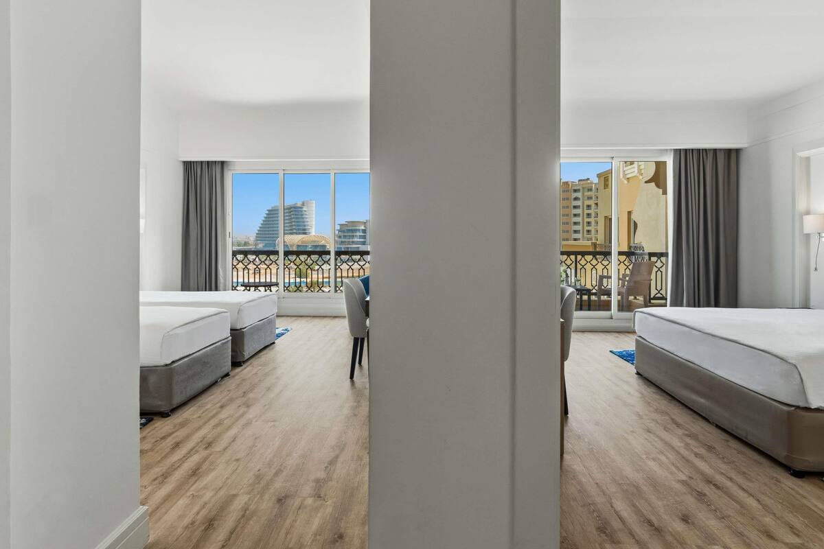 Habitación de hotel con dos camas, un balcón y vistas a edificios, además de piso de madera.