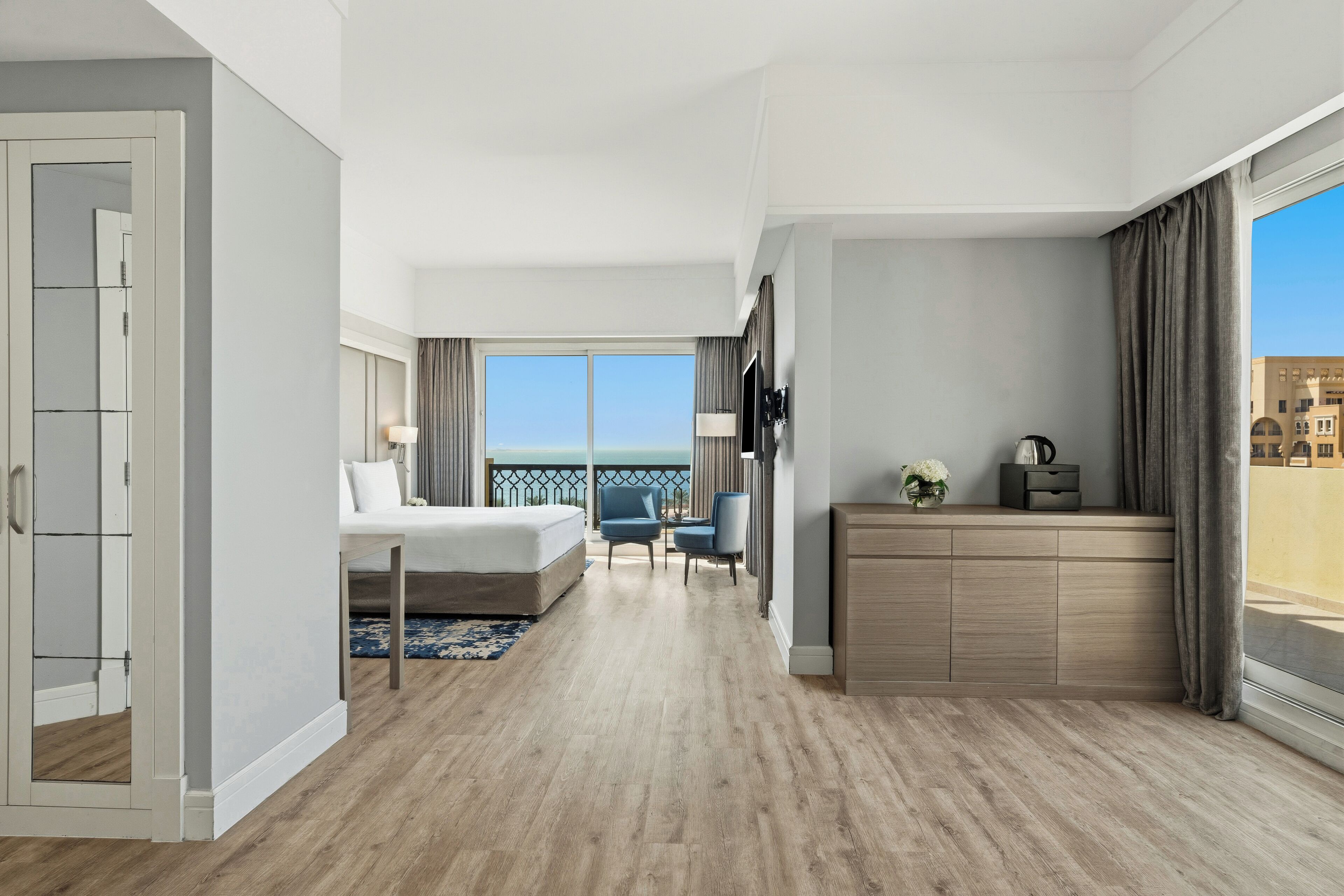 A modern hotel room with a large bed, a desk, a chair, and a balcony with a view.