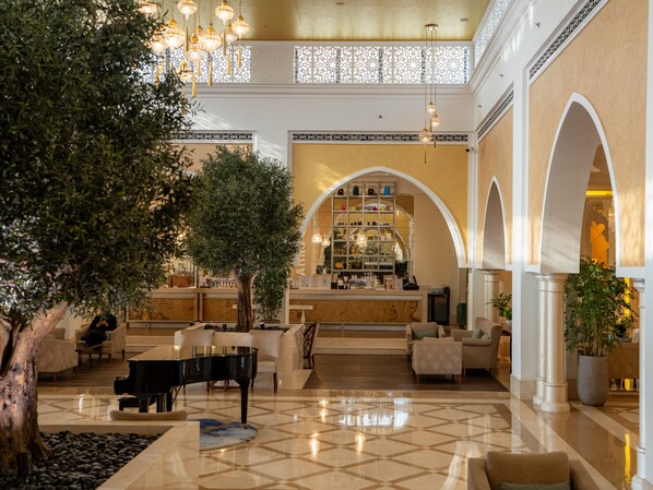 A spacious lobby with a grand piano, comfortable seating, a bar area, and a decorative tree. - Rixos Bab Al Bahr - All inclusive (Ras Al Khaimah)