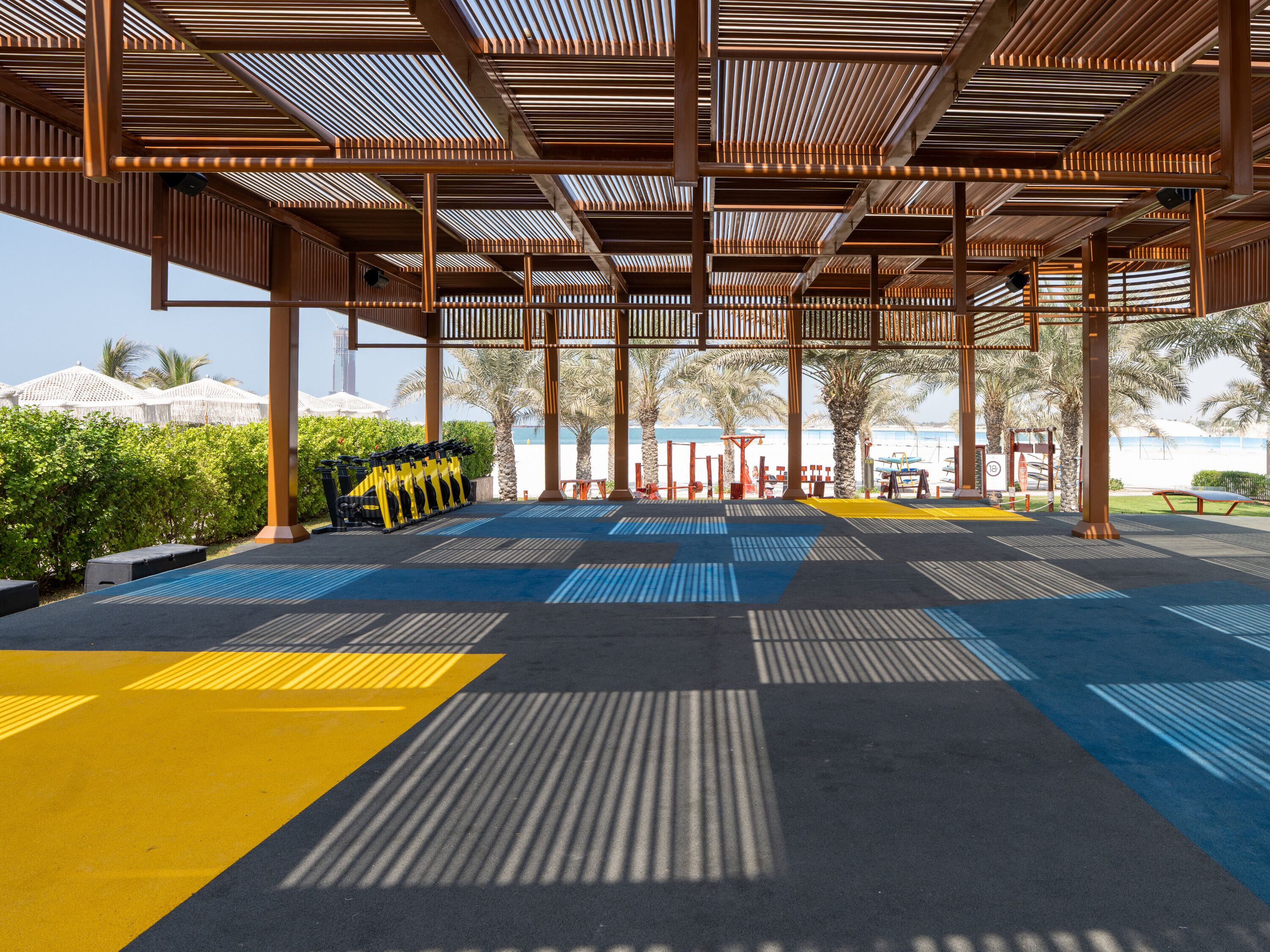 An outdoor gym area with exercise equipment, a patterned floor, and a wooden pergola structure.