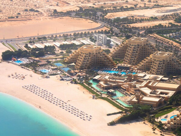 An aerial view of a resort with multiple buildings, a large pool area, and a beach with sun loungers. - Rixos Bab Al Bahr - All inclusive (Ras Al Khaimah)