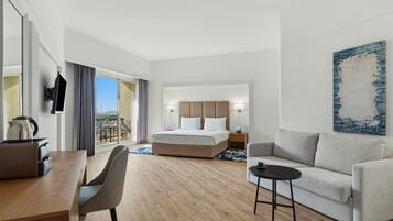 A hotel room with a bed, a desk, a chair, a sofa, a TV, and a painting.