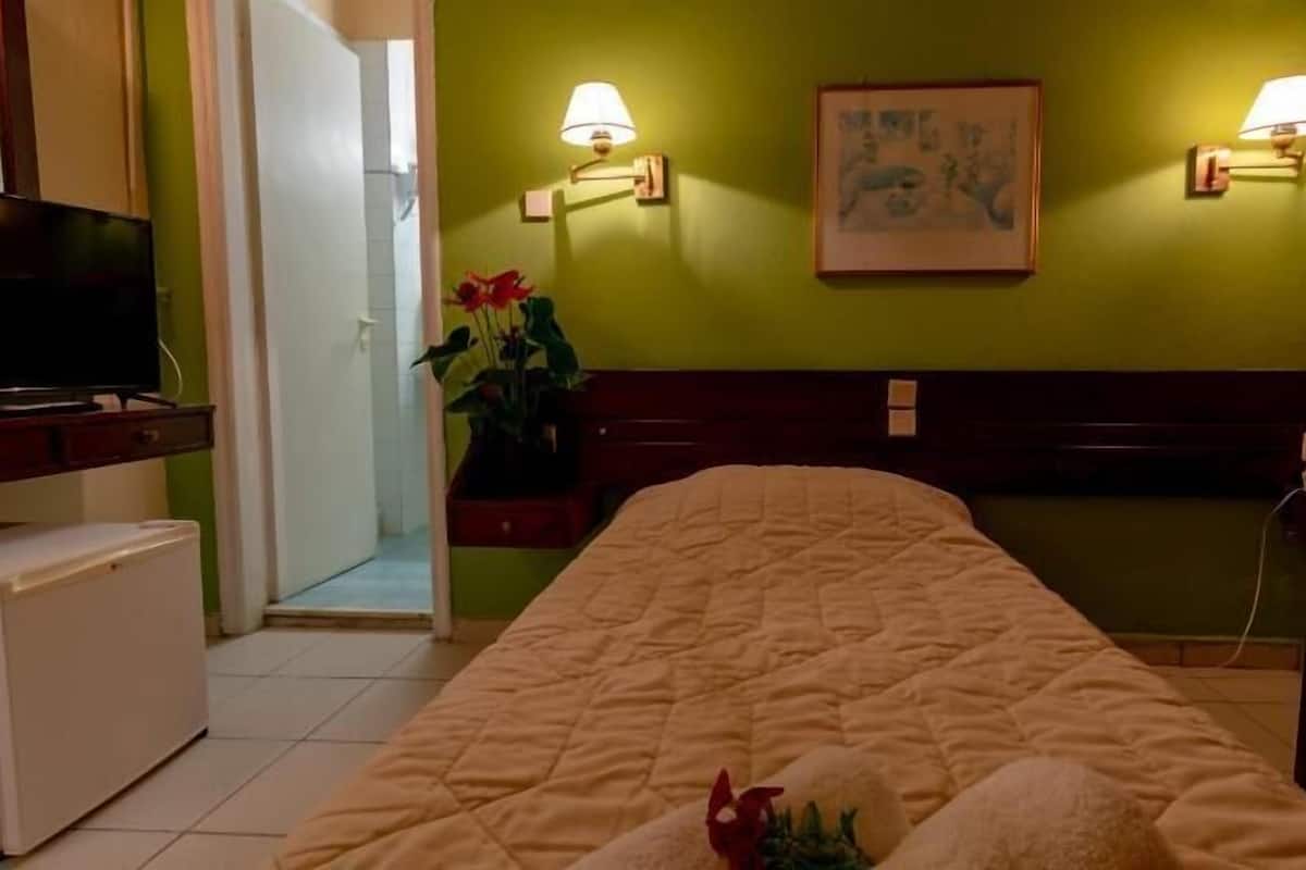 A hotel room with a bed, bedside tables, a TV, and a painting on the wall.