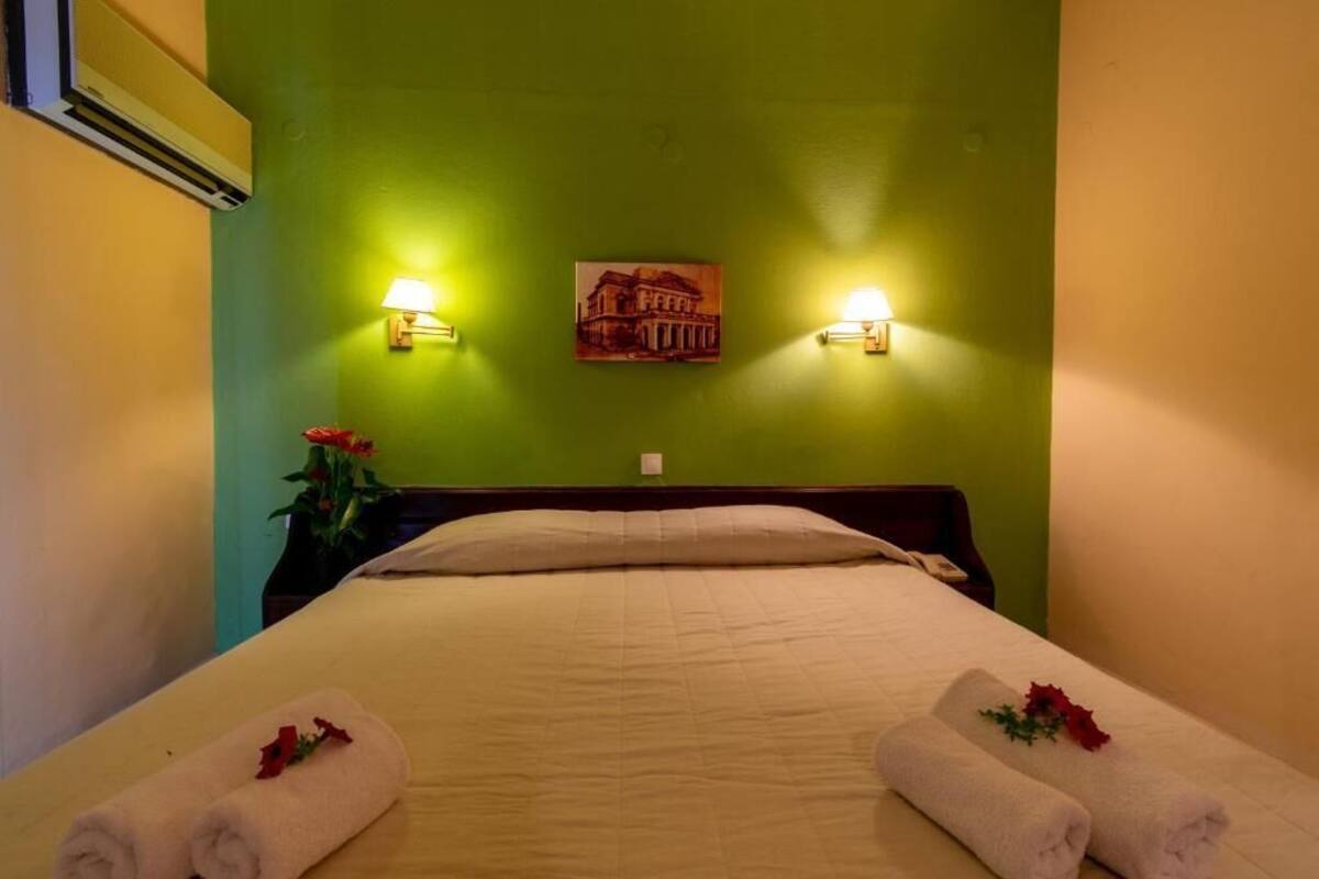 A hotel room with a bed, two wall-mounted lamps, a painting, and a vase with flowers.
