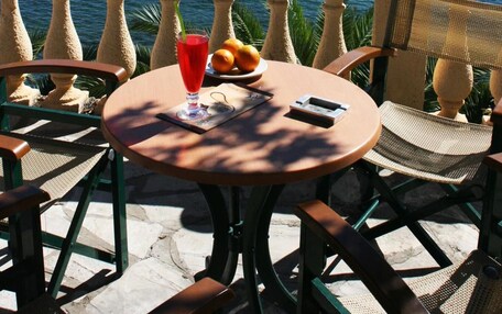 A table with a drink, fruit, and a phone on a balcony overlooking a body of water and a small island.