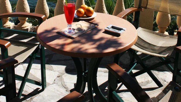 A table with a drink, fruit, and a phone on a balcony overlooking a body of water and a small island. - Aegli Hotel (Corfu)