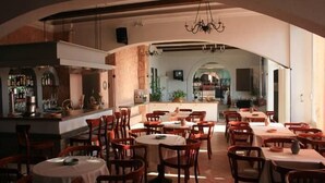 A restaurant with round tables and wooden chairs, an arched ceiling, and a bar area visible in the background. - Aegli Hotel (Corfu)