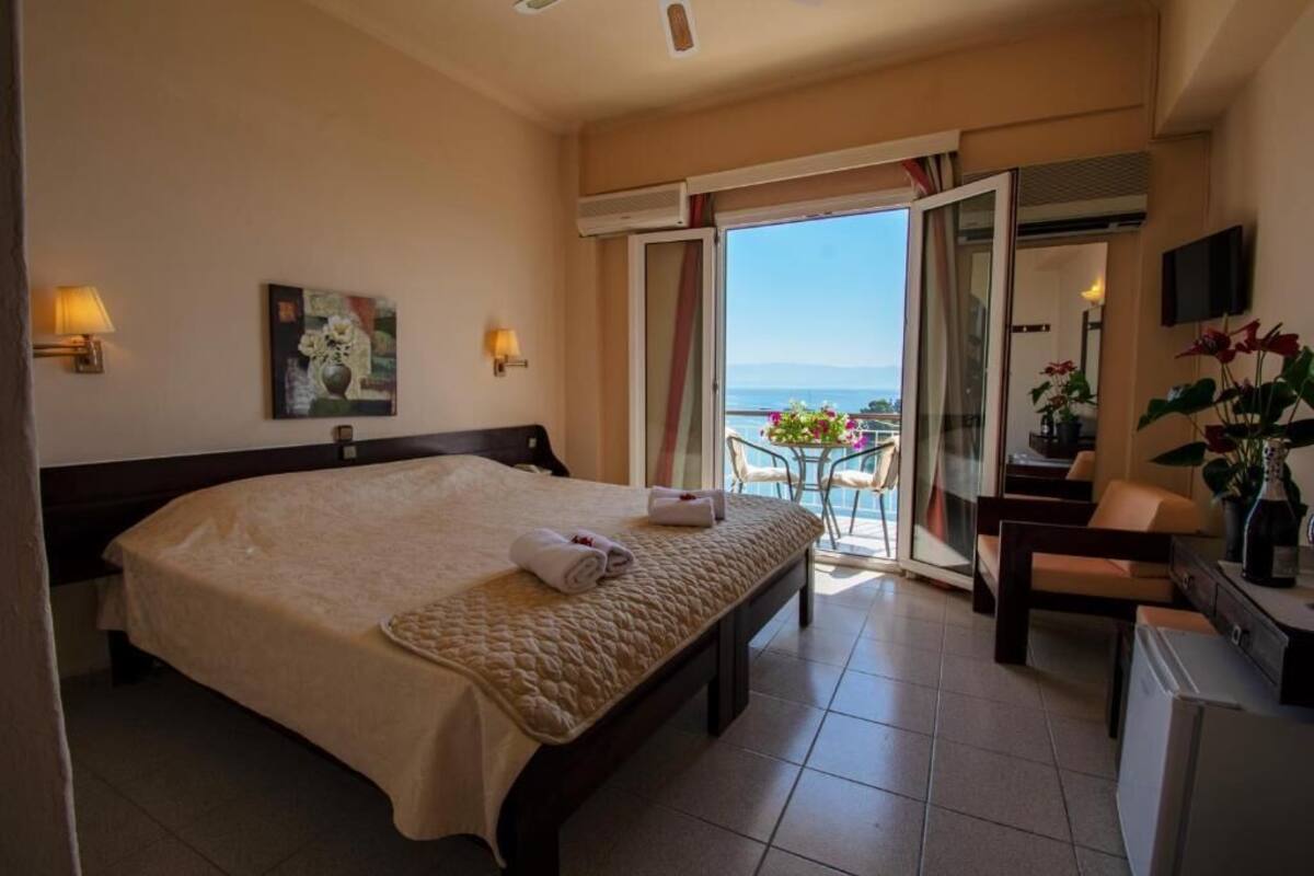 A hotel room with a bed, a desk, a chair, a TV, and a balcony with a view.