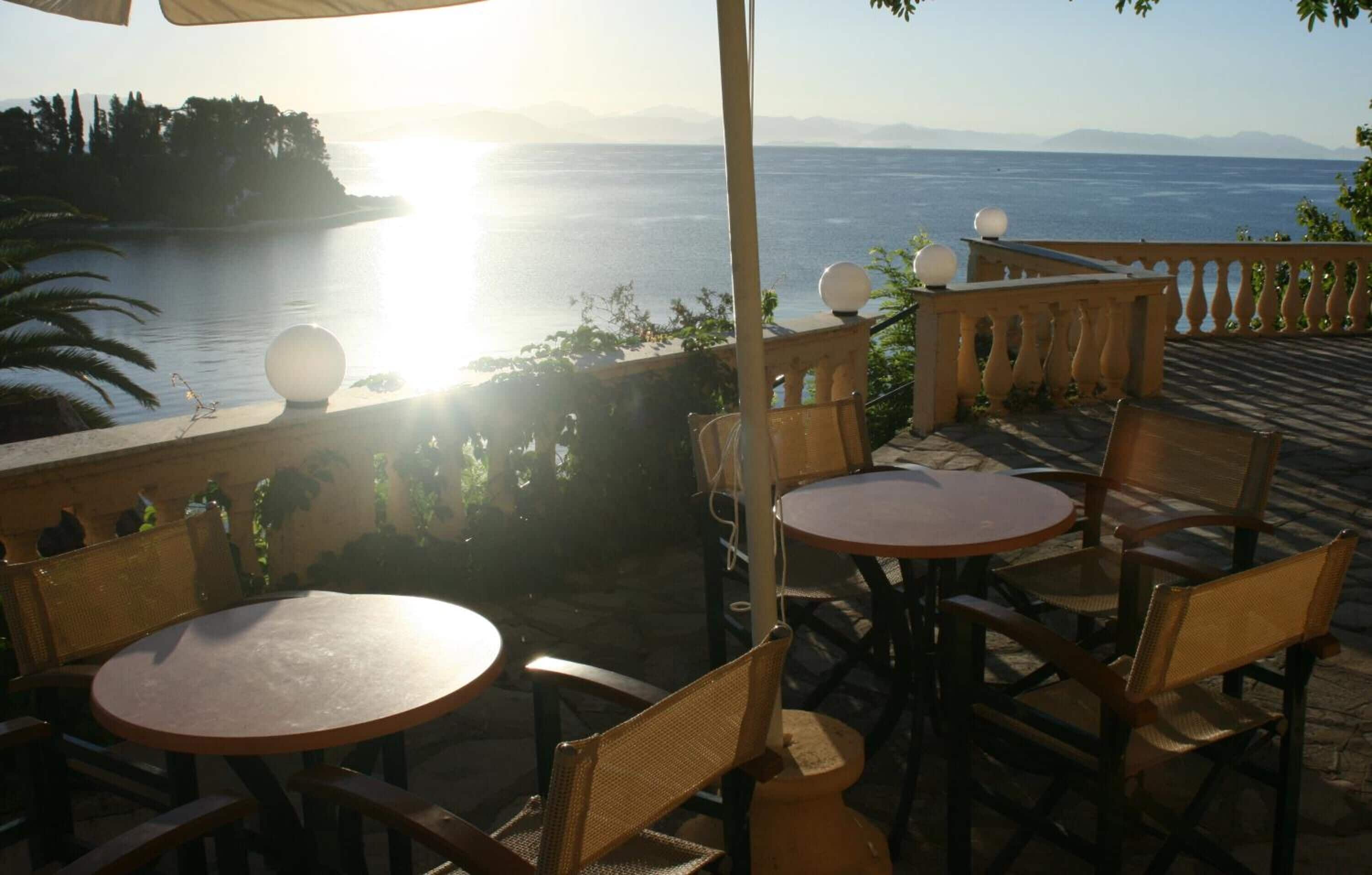 An outdoor seating area with round tables and chairs, overlooking a body of water and distant mountains.