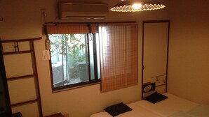 A bedroom with a bed, a bedside table, a wardrobe, a window with blinds, and an air conditioning unit. - Hanakiya (Kyoto)