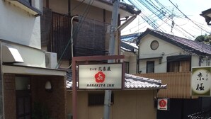 A building with a sign for Hanakiya Inn, featuring a traditional Japanese architectural style with a tiled roof and a small entrance area with potted plants. - Hanakiya (Kyoto)