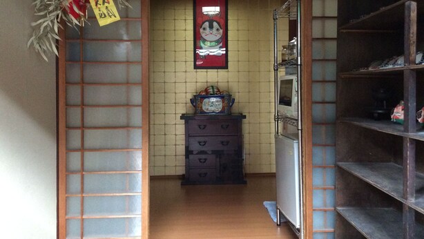 A narrow hallway with a traditional Japanese-style sliding door, a small cabinet with decorative items, and a shelf unit to the right. - Hanakiya (Kyoto)