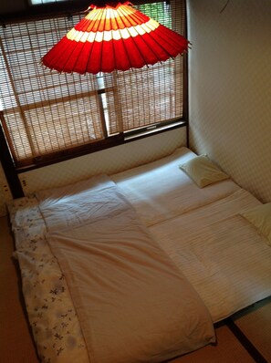 Una cama individual con colcha blanca y estampada, cabecera de madera y lámpara colgante roja.