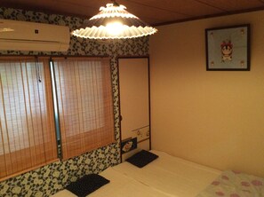 Una habitación con cama, ventana con persianas, aire acondicionado de pared, una lámpara decorativa y un cuadro enmarcado en la pared.
