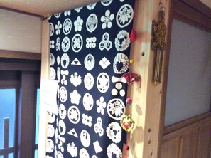 A room with a patterned curtain, a wooden door, and a wall-mounted decoration. - TANAKA-ya (Kyoto)