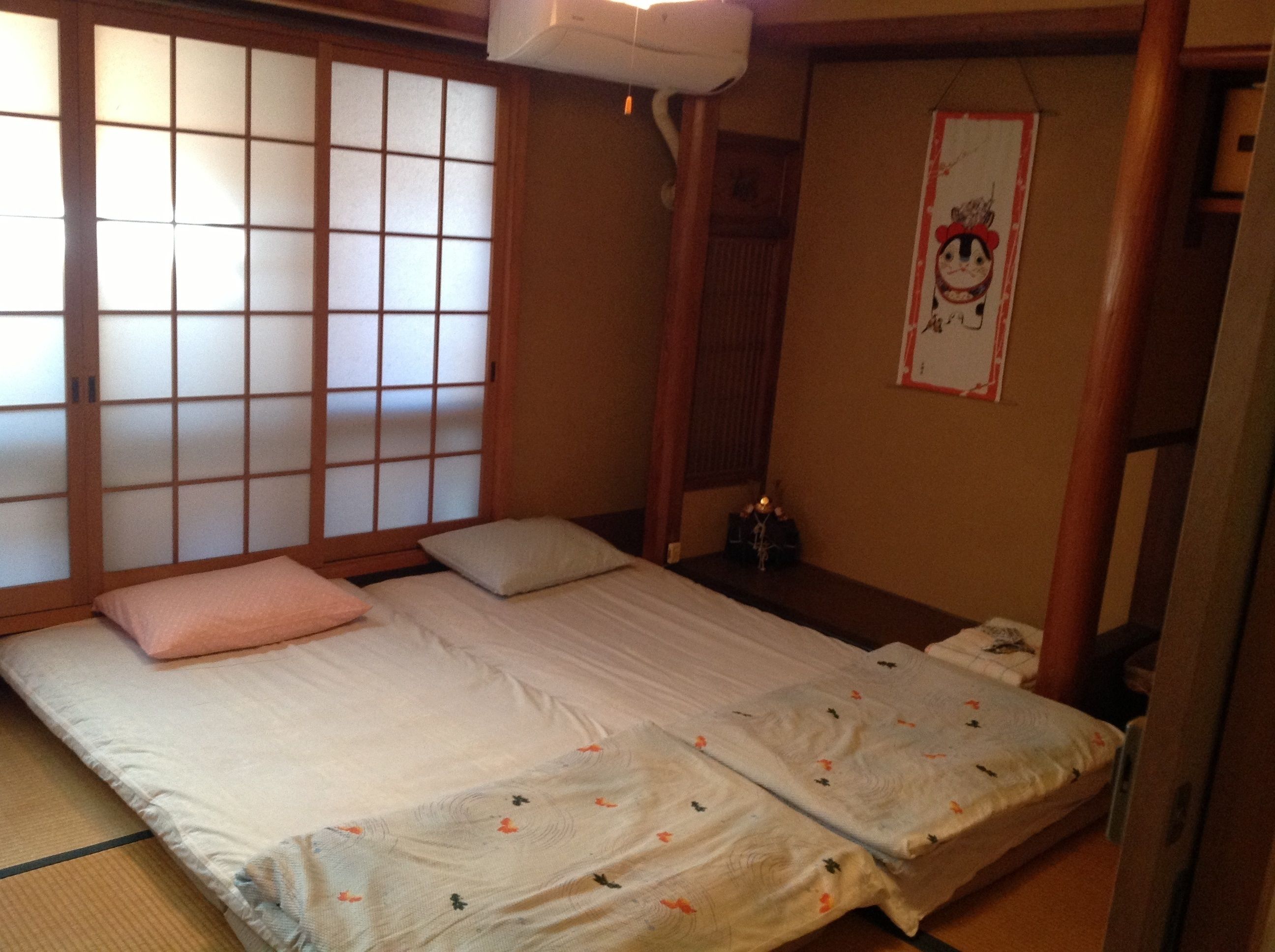 A traditional Japanese room with tatami flooring, a low bed with a futon, sliding shoji doors, and a small shrine with a candle.