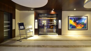 A hotel lobby with a reception desk, a glass door entrance, and a large abstract painting on the wall. - Rivatas (Varanasi)