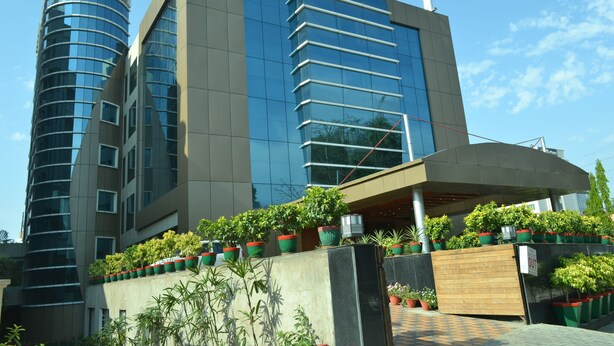 A modern building with a curved glass facade, a flat roof, and a series of potted plants along the front.